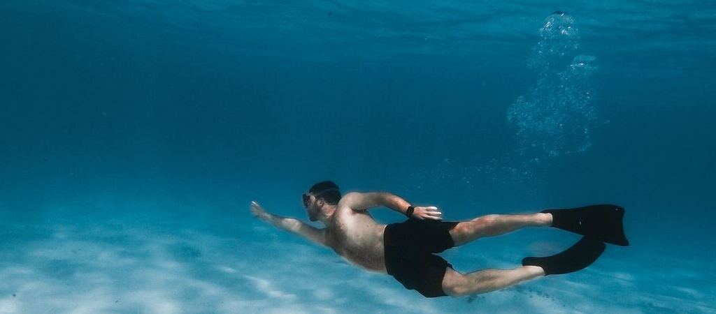 Symbolic image “Curaçao snorkeling”: Man dives under water. He is wearing flippers and diving goggles.