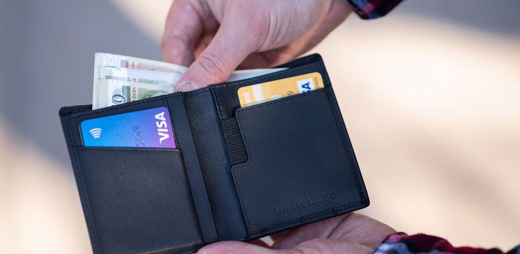 Symbolic image “Curaçao currency”: Man holds a black wallet in his hand and takes out a banknote.