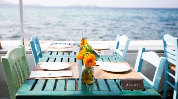 Symbolbild "Restaurant Curaçao": Ein Tisch mit vier bunten Stühlen steht auf einer Terrasse eines Restaurants. Von dort aus hat man einen hervorragenden Blick auf Meer.