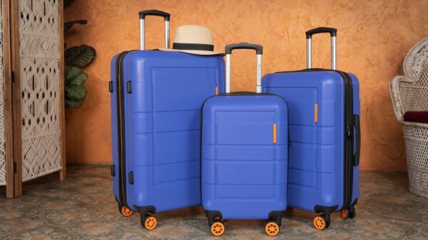 Symbolic image "baggage insurance": Three blue suitcases in different sizes stand in front of an orange-colored wall.