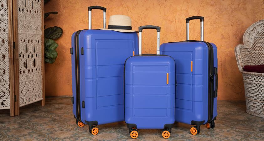 Symbolic image "baggage insurance": Three blue suitcases in different sizes stand in front of an orange-colored wall.