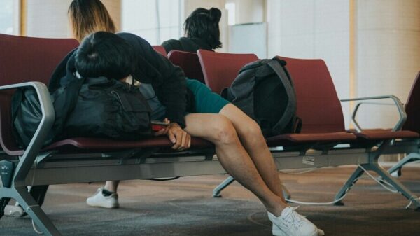 Symbolbild "Jetlag überwinden": Person schläft auf roter Sitzbank am Flughafen.