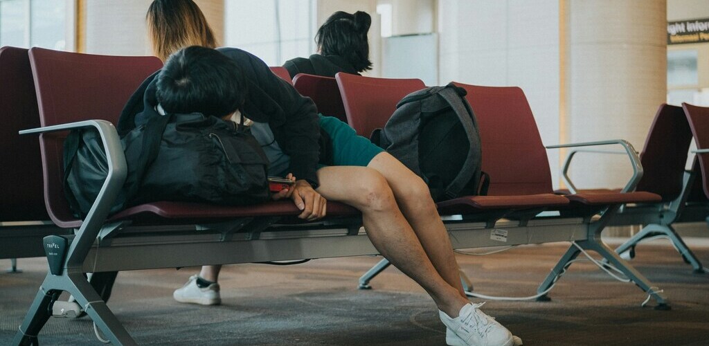 Symbolic image “How to Get Over Jet Lag”: Person Sleeping on a Red Bench at the Airport.