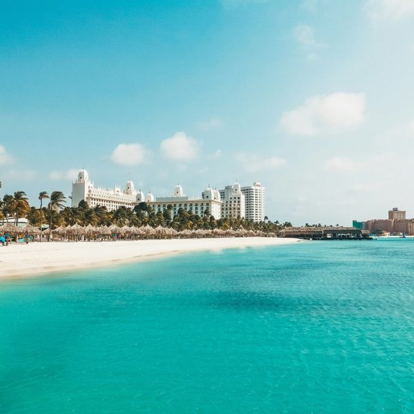 Aussicht auf eine Hotelanlage am Palm Beach auf Aruba, einer Niederländischen Karibikinseln. Im Vordergrund sieht man das blaue Meer und links davon einen weißen Sandstrand.