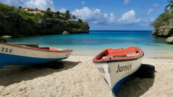 Two colorful boats stand on the edge of Playa Lagun in Curaçao. The turquoise sea can be seen in the background.