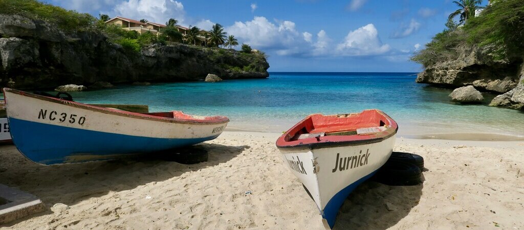 Zwei bunte Boote stehen am Rande des Playa Lagun auf Curaçao. Im Hintergrund ist das türkisfarbene Meer zu sehen.